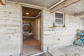 L’intérieur d’un chalet rustique en bois, avec des poutres apparentes, une fenêtre à cadre blanc et une porte donnant sur une autre pièce.