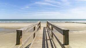 Une promenade en bois menant à une plage, avec un ciel dégagé.