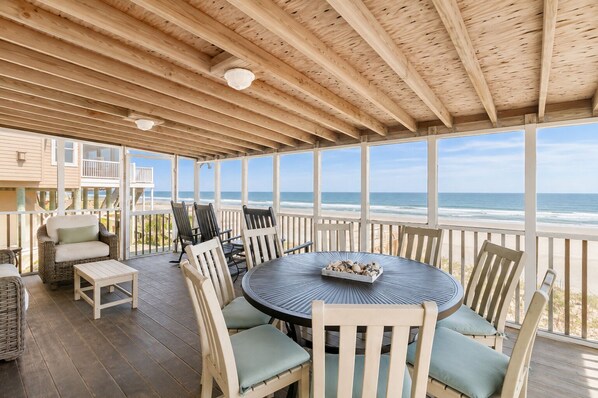 A covered outdoor seating area with a view of the ocean, featuring a round table and chairs.