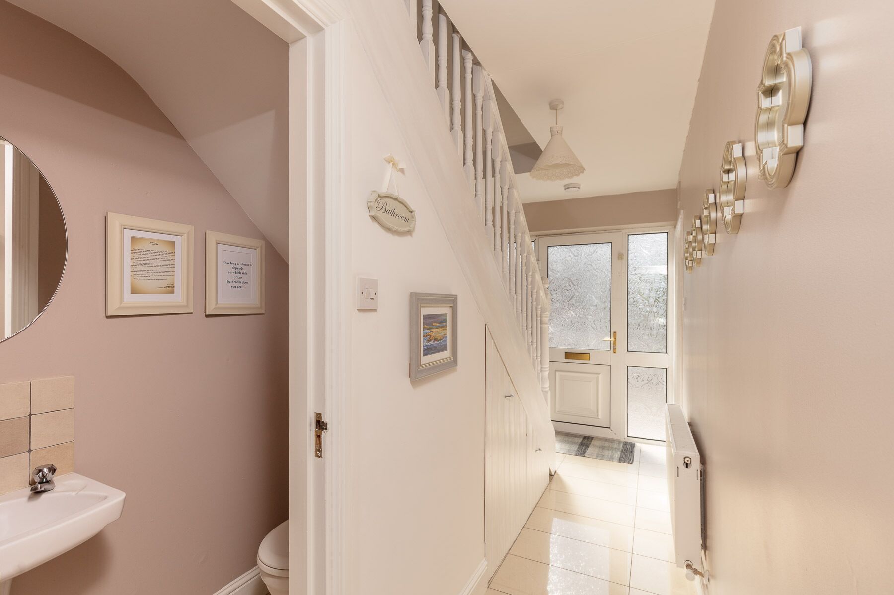 Un couloir menant à une salle de bain équipée d’un lavabo, ornée de citations encadrées, et donnant sur un escalier.