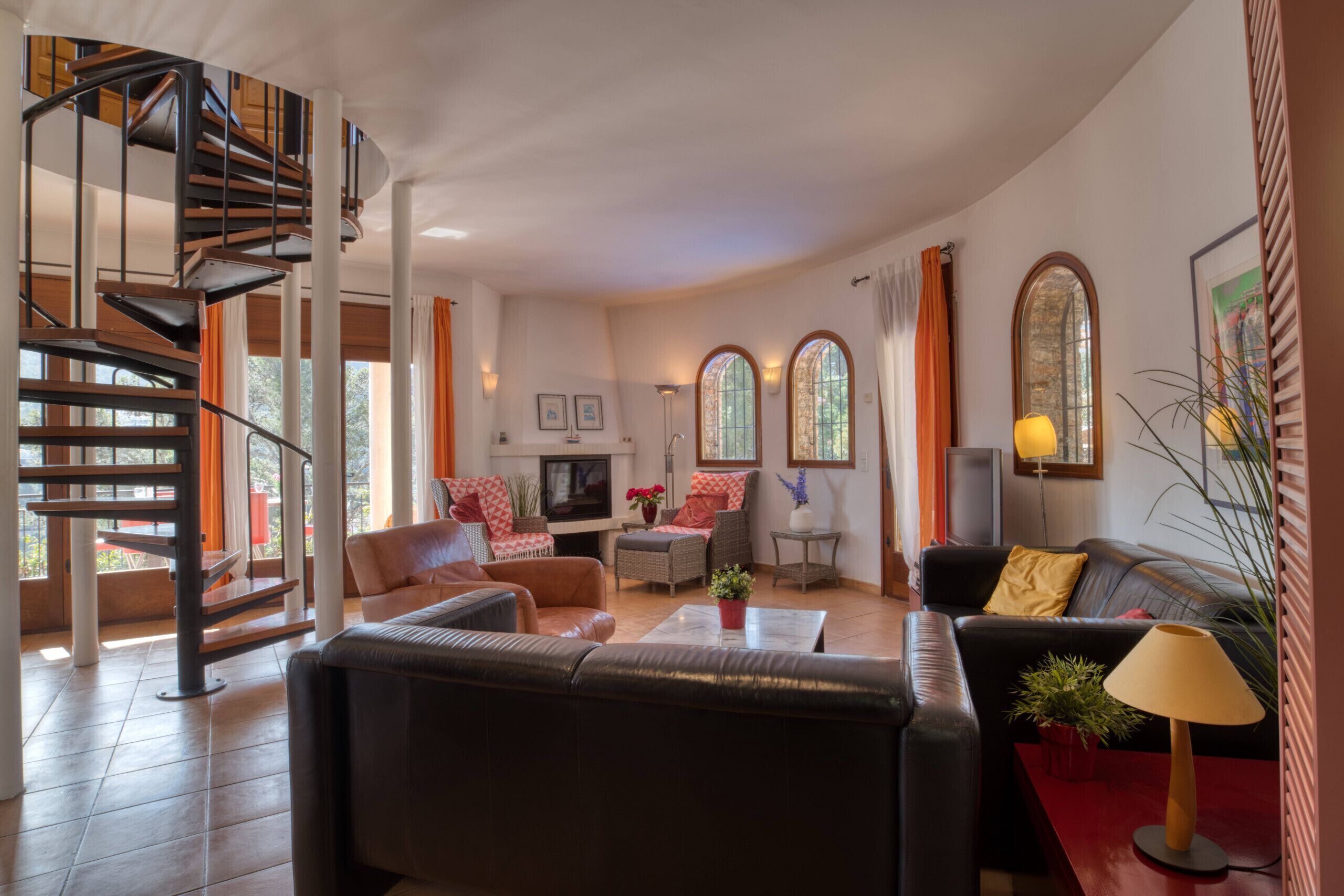 A modern living room with a spiral staircase, leather sofas, a coffee table, and a TV.