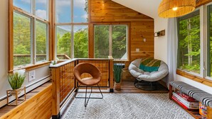 A cozy cabin interior with large windows, wooden walls, a cushioned chair, a bench, and a hanging light fixture. - Secluded/Hot Tub/views! Minutes to Everything! (Bridgewater Corners)