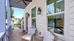 A covered porch with wicker chairs and a ceiling fan, large windows, and a view of the neighborhood.