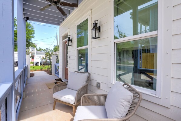 A covered porch with wicker chairs and a ceiling fan, large windows, and a view of the neighborhood.