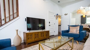 A living room with a television, a blue sofa, a glass coffee table, and a patterned rug.