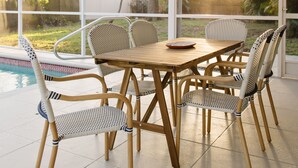 Une terrasse couverte, avec une table en bois et des chaises en osier, donnant sur une piscine et un jardin arboré.