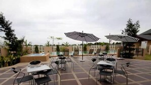 An outdoor patio with tables and chairs, umbrellas, and a pool area.