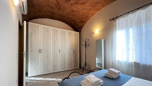A bedroom with a bed, a wardrobe, a coat rack, and a window with curtains.