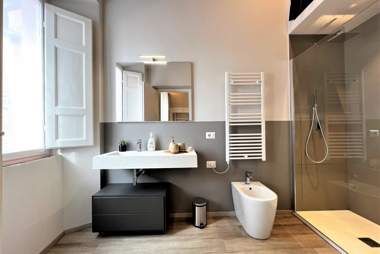 Un baño moderno con tocador blanco, un mueble negro, un bidé y una mampara de vidrio.