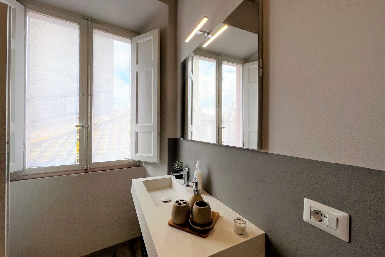 Un baño moderno con un ventanal grande, un lavamanos con espejo y una planta pequeña en la encimera.