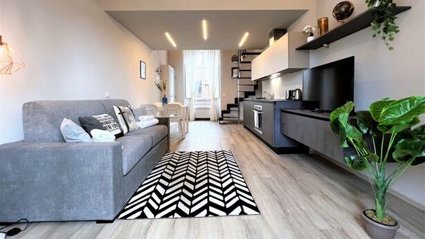 Ein modernes Wohnzimmer mit einem grauen Sofa, einem schwarz-weißen Teppich und einem Fernseher.