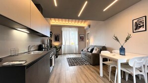 Eine moderne Küche mit einer zentralen Kochinsel, ein Essbereich mit einem weißen Tisch und Stühlen, sowie ein Wohnbereich mit einer Couch und einem Couchtisch.