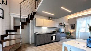 Eine moderne Küche mit einer zentralen Kochinsel, einer Treppe und einem Essbereich mit weißem Tisch und Stühlen.
