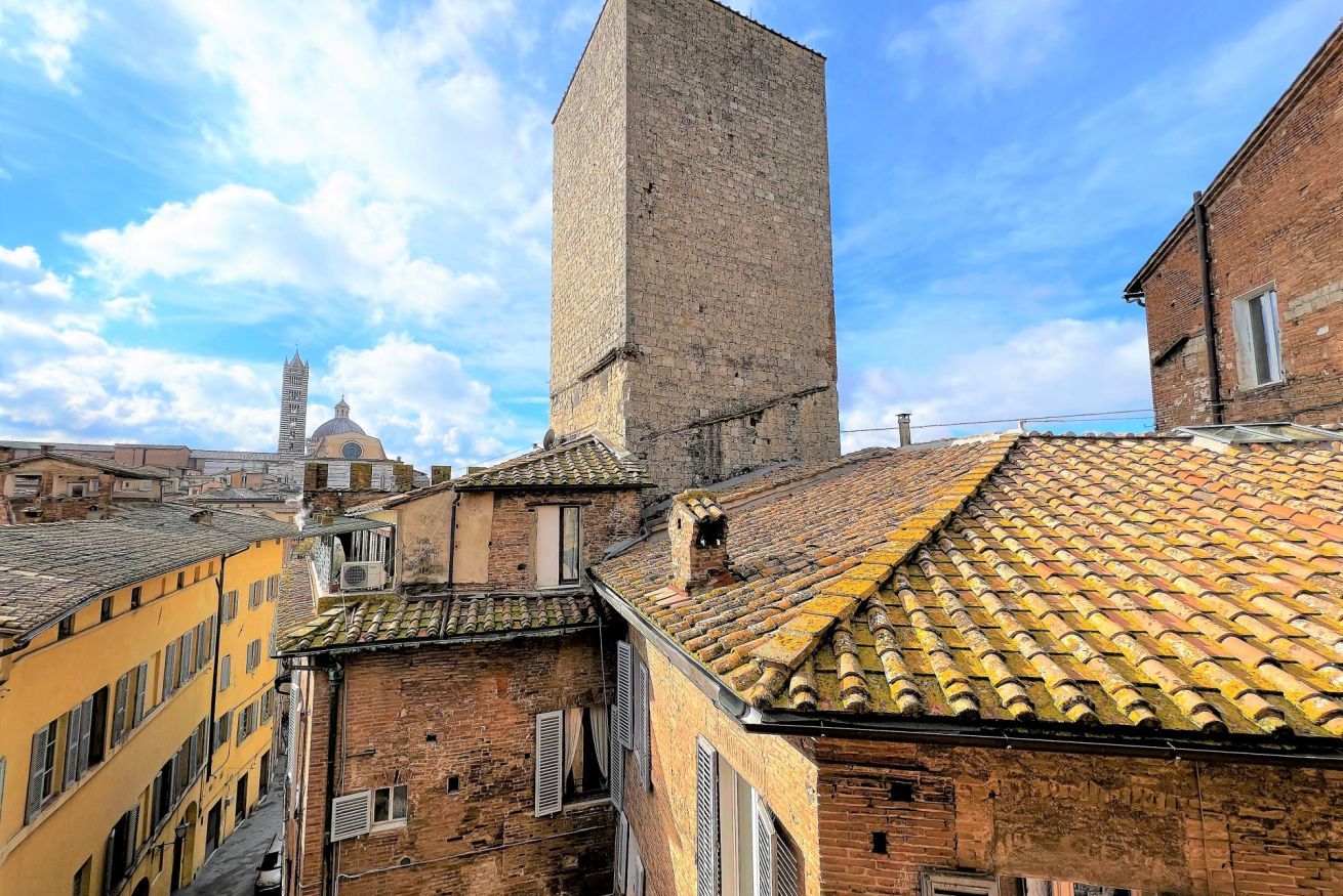 A historic building with a prominent tower, adjacent traditional buildings, and a dome in the background.