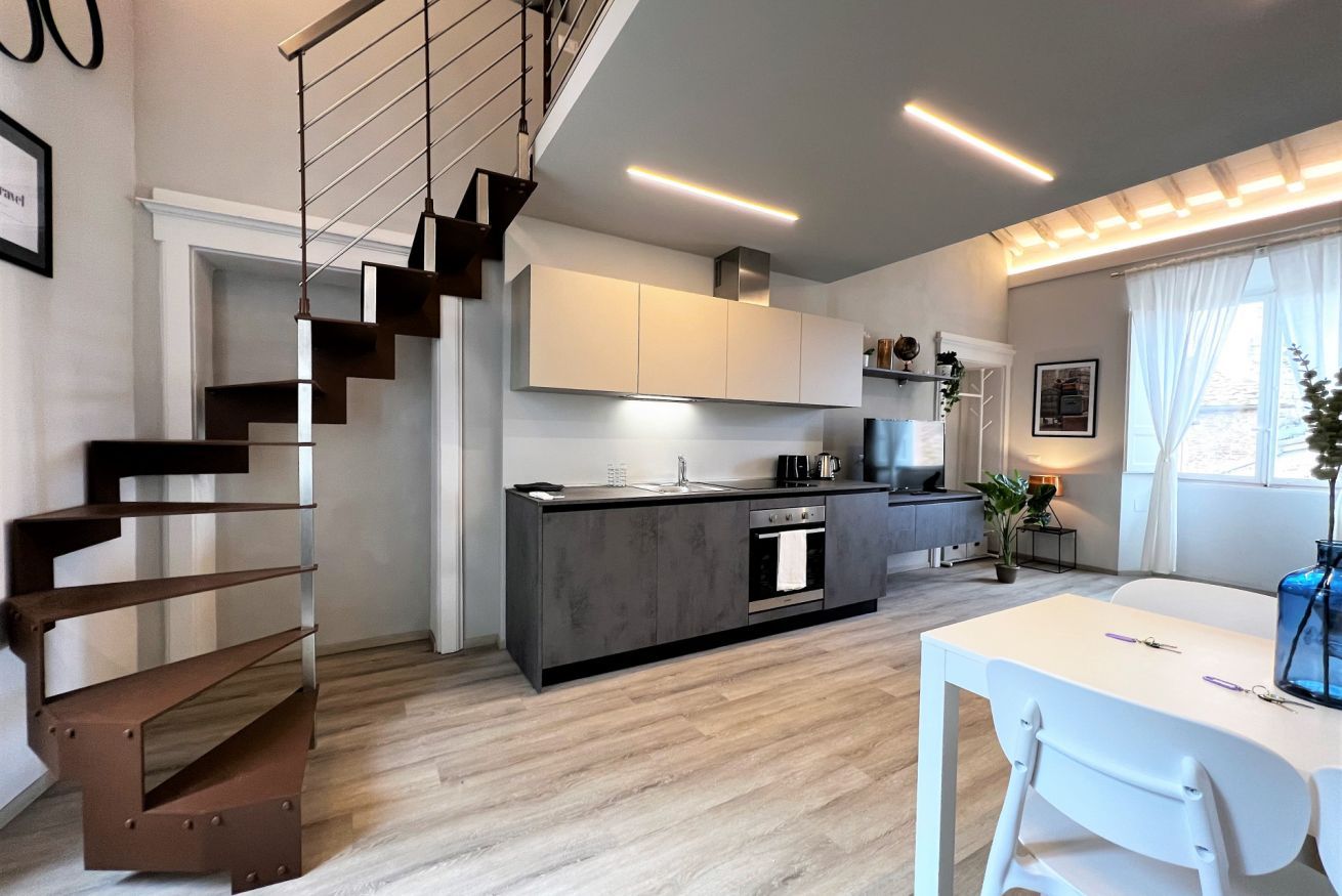A modern kitchen with a central island, a staircase, and a dining area with a white table and chairs.