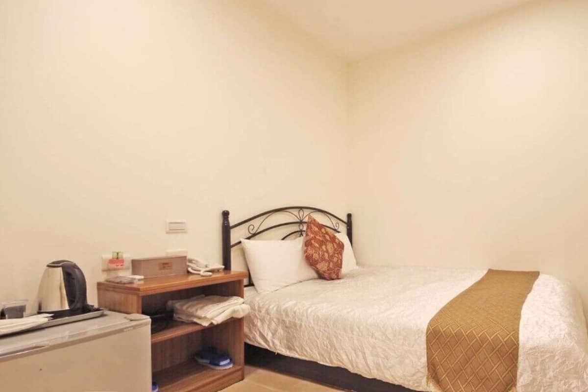 Een compacte, keurig ingerichte slaapkamer met een eenpersoonsbed, een nachtkastje, een bureau en een stoel.