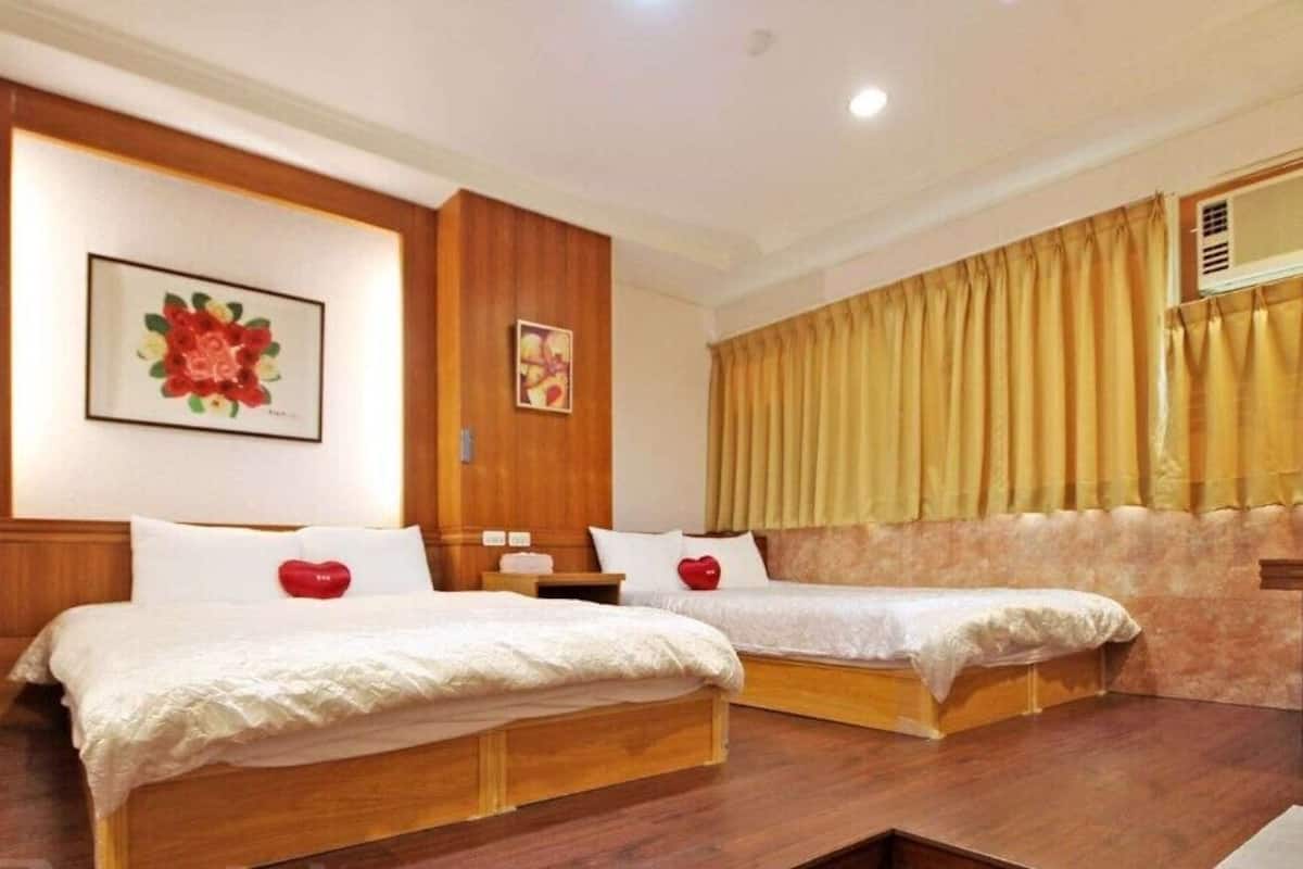 Hotelkamer met twee bedden, houten hoofdeinden, een groot bloemenkunstwerk aan de muur, en een raam met gordijnen.