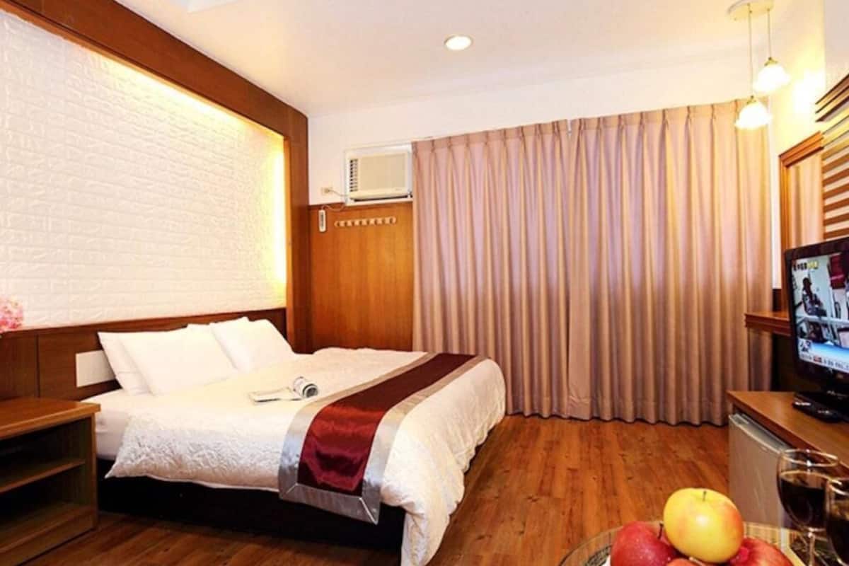 Een hotelkamer met een bed, een televisie, een houten bureau en een schaal fruit.
