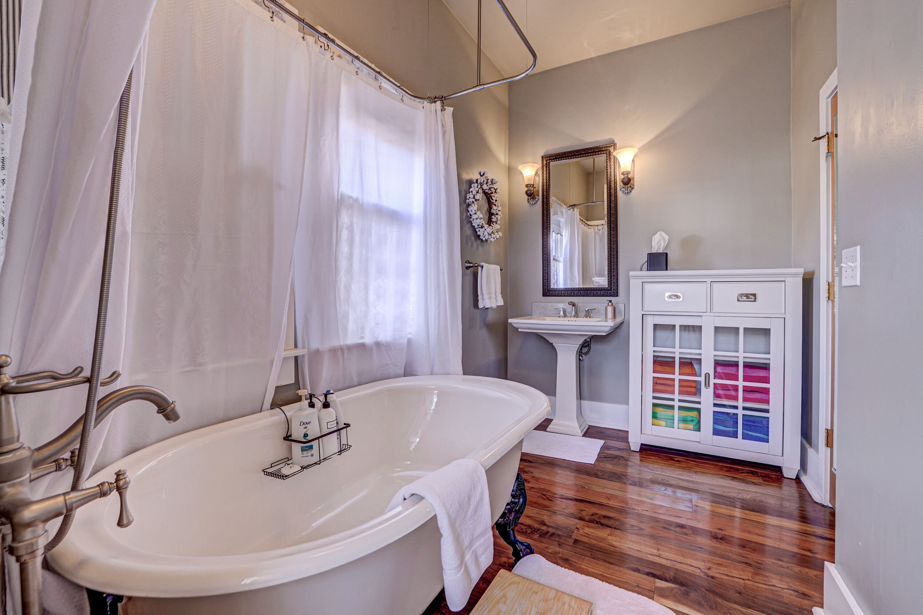 A bathroom with a freestanding bathtub, a pedestal sink, a vanity with a mirror, and a cabinet with storage drawers.