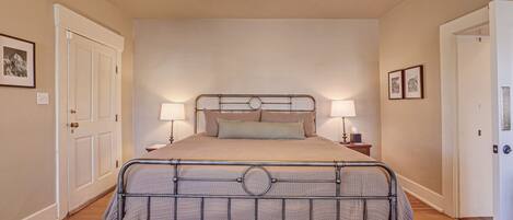 Ein Schlafzimmer mit einem Metallbettgestell, zwei Nachttischlampen, einem gemusterten Teppich und einer Deckenleuchte.