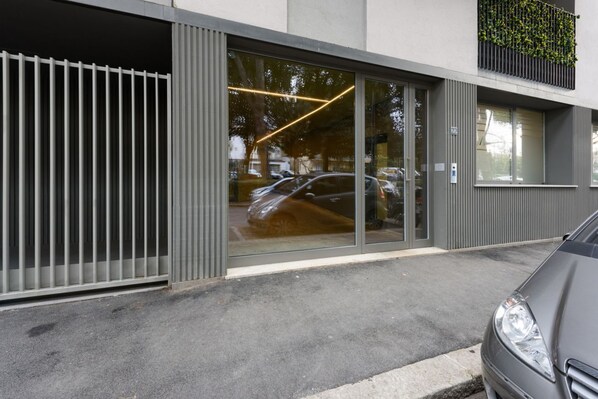 A modern building entrance with a glass door, metal railing, and a car parked outside.
