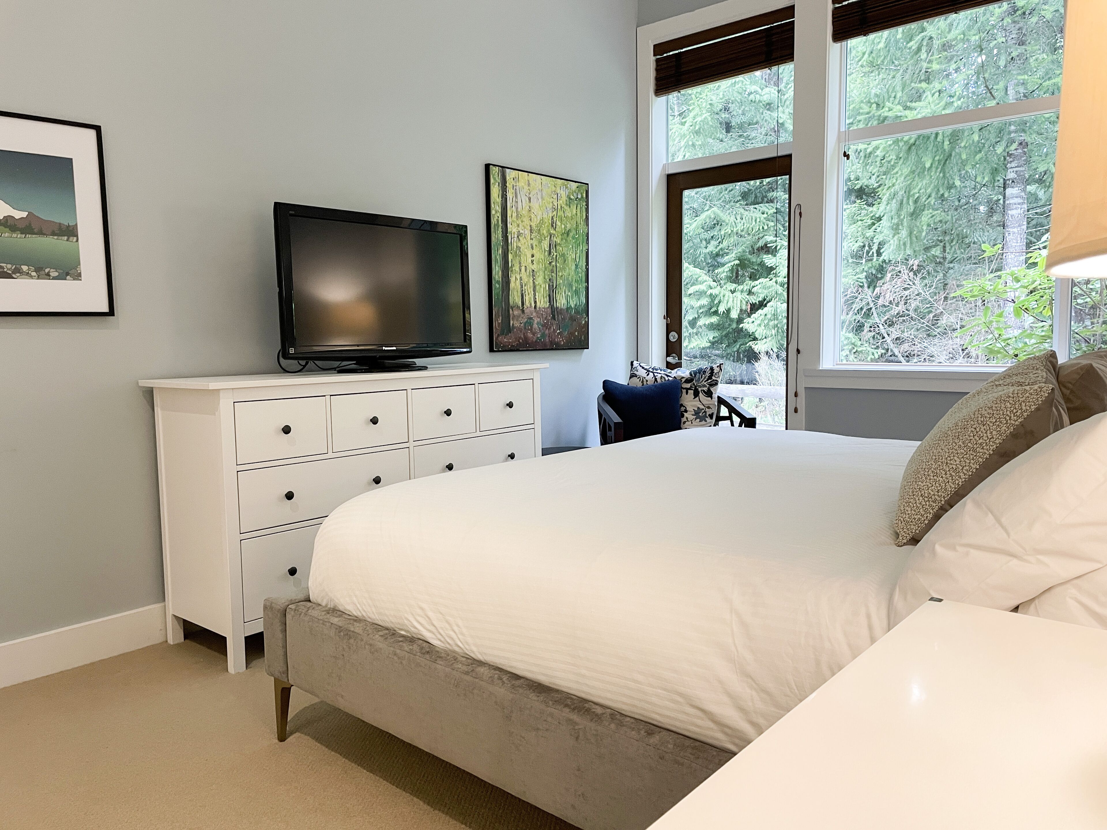 A bedroom with a bed, a dresser, a television, and a window with a view of trees.