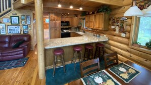 A wooden cabin interior with a kitchen, dining area, and a living room with a couch. - Kenai riverfront log cabin, perfect for fishing, close to town (Sterling)