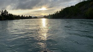 A river with a boat in the foreground, surrounded by trees and a cloudy sky. - Kenai riverfront log cabin, perfect for fishing, close to town (Sterling)