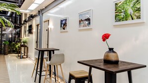 A modern interior with a clean, white wall adorned with framed photographs, a wooden table with a vase of red flowers, and a seating area with chairs and a small stool. - MORIYAMA HOTEL (Mandaue)