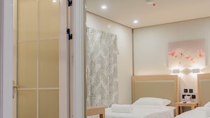 A hotel room with three beds, a wooden floor, a sliding door, and a wall-mounted light fixture. - MORIYAMA HOTEL (Mandaue)
