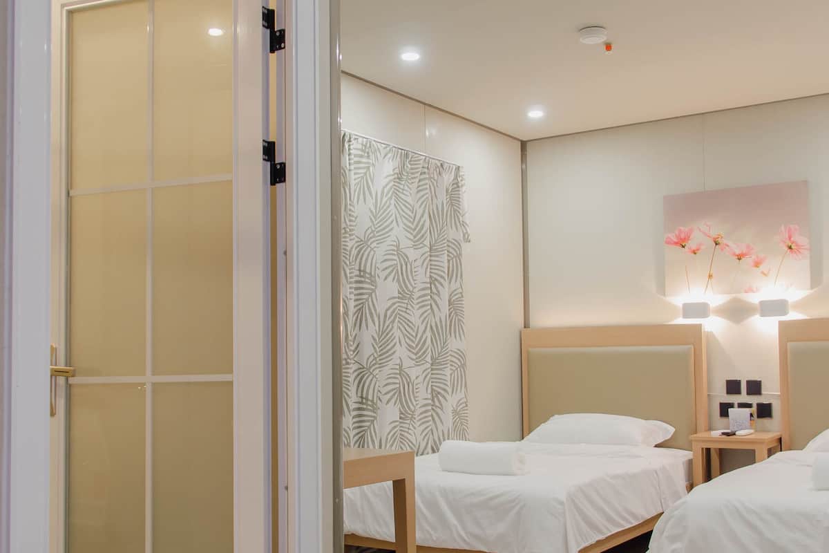Habitación de hotel con tres camas, piso de madera, puerta corredera y una lámpara fijada a la pared.