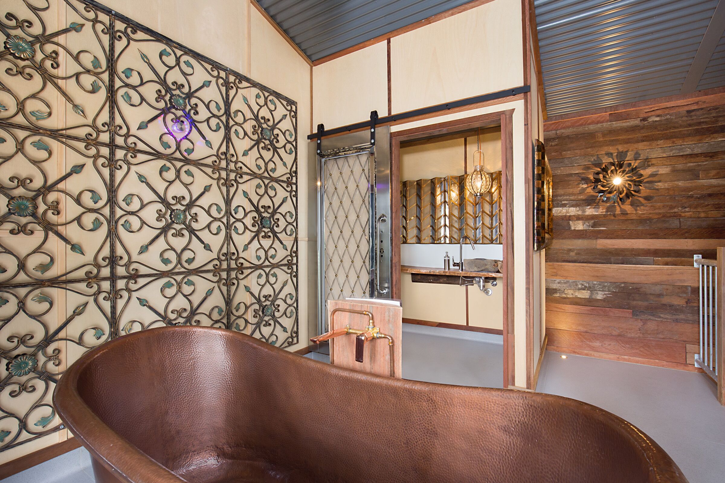 Un baño con una bañera independiente, una pared de madera con un panel metálico decorativo y un espejo con marco de madera.