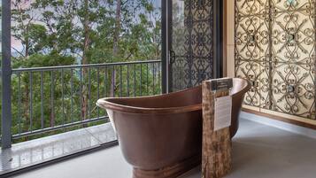 A large, antique-style bathtub in a room with a balcony overlooking trees.