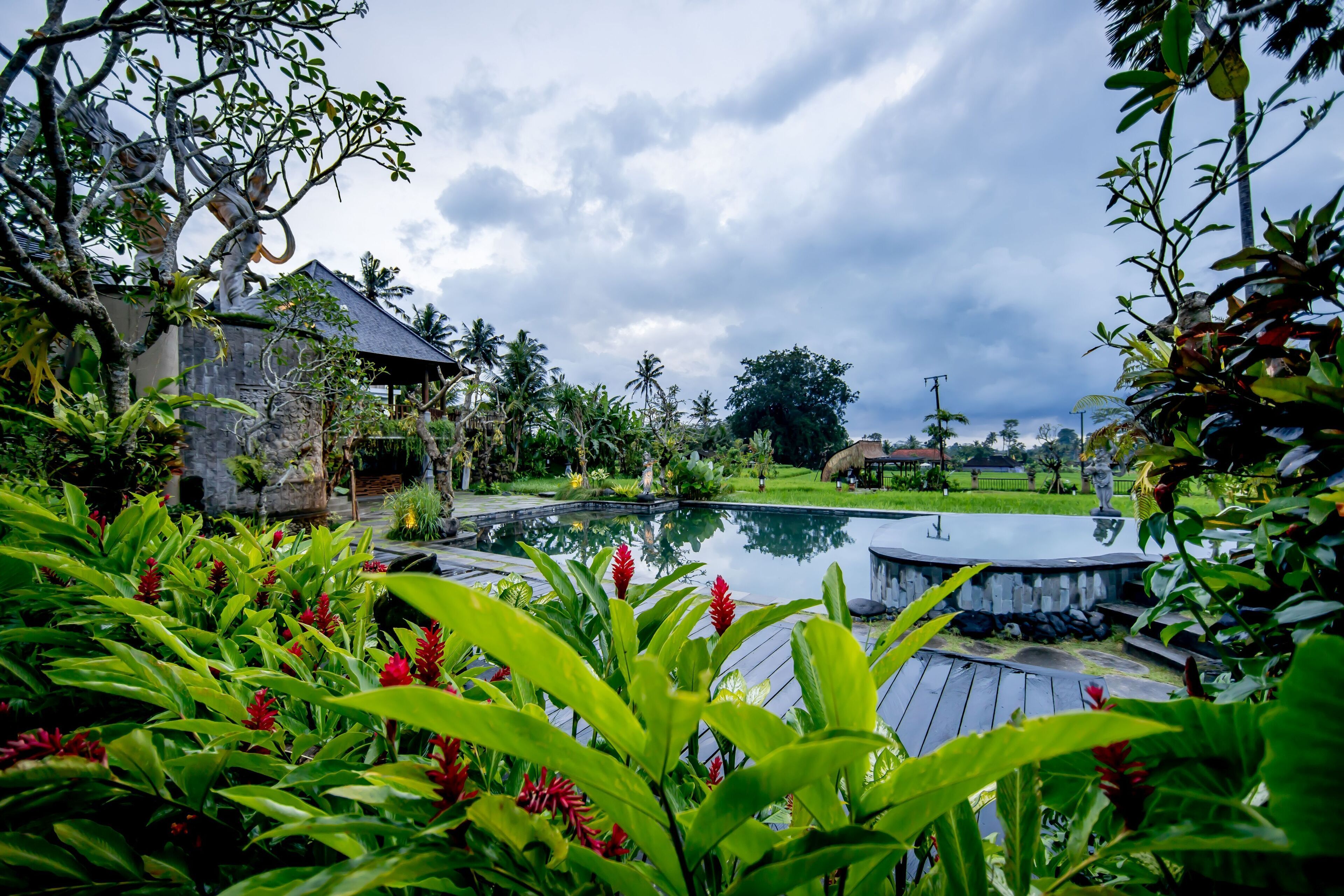 A pool area with a stone structure, surrounded by lush greenery and a cloudy sky.