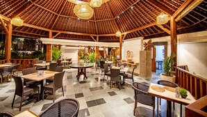 Un vaste espace intérieur doté de poutres en bois au plafond, de nombreuses tables et chaises, et de lampes en osier suspendues.