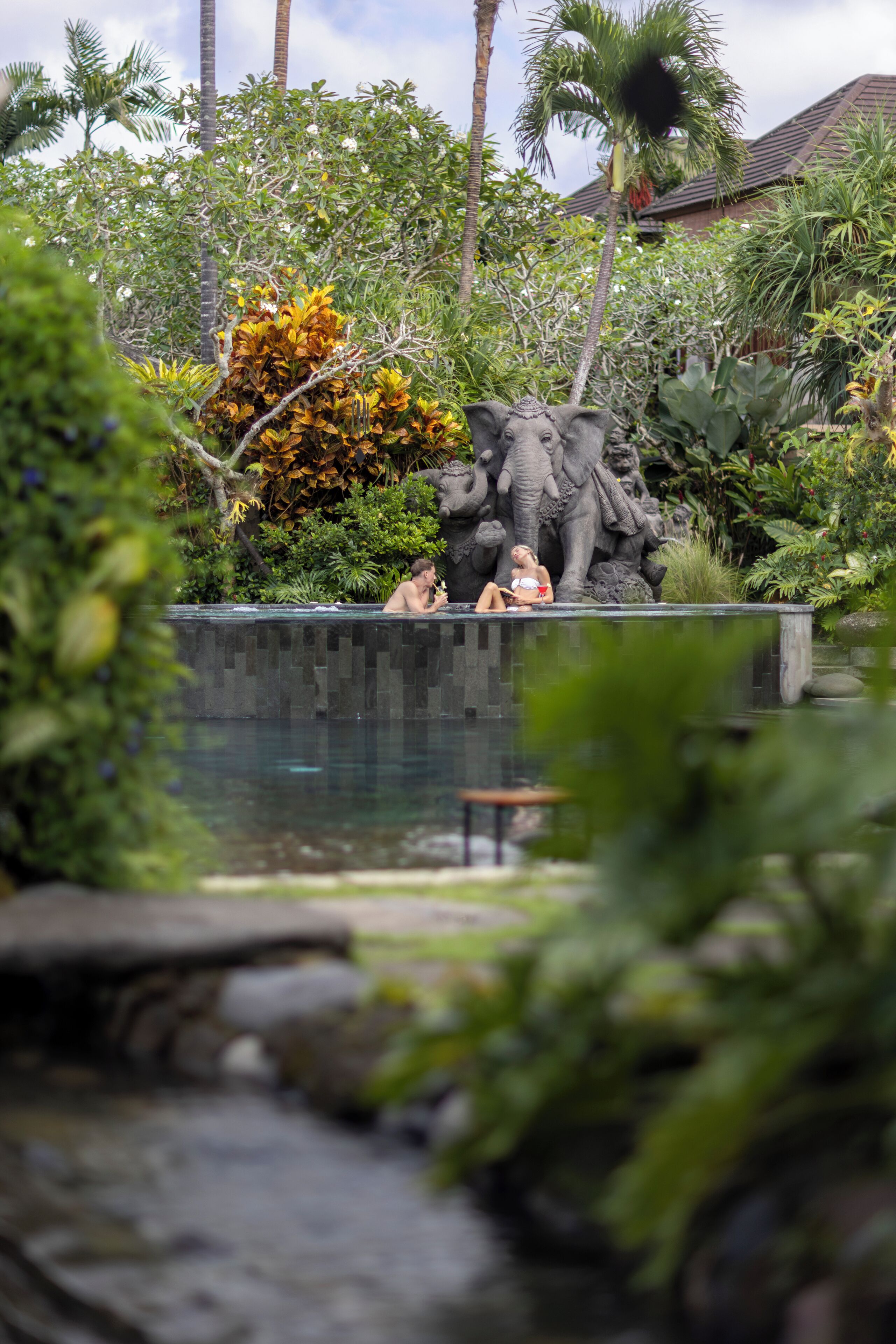 Zona de piscina con una estatua de elefantes y plantas tropicales.