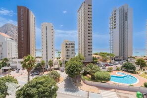 Un immeuble résidentiel de grande hauteur doté d’une piscine, de palmiers et offrant une vue dégagée sur la mer.