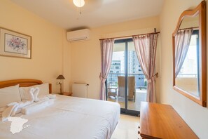 Une chambre d’hôtel avec un lit, une commode en bois, une chaise et une vue sur le balcon extérieur.
