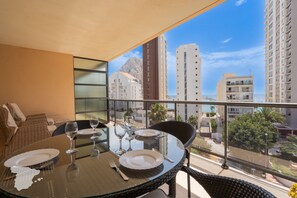 Un balcon avec une table à manger pour deux personnes, d’où l’on peut admirer un panorama urbain avec de hauts immeubles et un ciel dégagé.