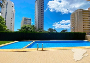 A swimming pool with a wooden deck, surrounded by tall residential buildings and greenery.