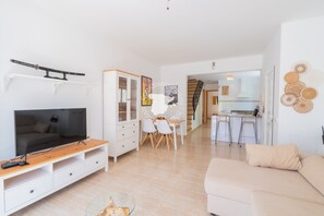 A modern living room with a TV, wooden entertainment unit, white sofa, dining area with chairs, and a kitchen in the background. - CostaBlancaDreams - Casa Alis in Calpe (Calpe / Calp)