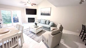A living room with a sofa, coffee table, and chairs. There is a fireplace, a ceiling fan, and a TV mounted on the wall. - Tempe town house near ASU. only 2 miles away. (Tempe)