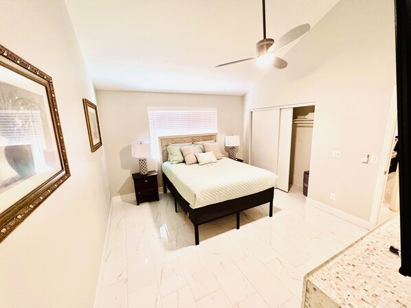 A bedroom with a bed, nightstands, a ceiling fan, a wardrobe, and a window with blinds.