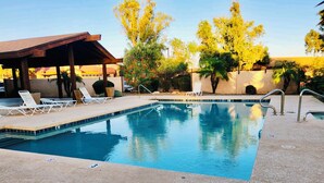 A swimming pool with lounge chairs, a covered seating area, and trees in the background. - Tempe town house near ASU. only 2 miles away. (Tempe)