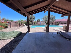 Un espacio al aire libre techado con piscina, sillas de descanso y una pérgola de madera.