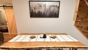 A wooden dining table with two chairs, a framed picture of a forest, and a coffee mug on the table. - Ellijay Mountain Escape with Private Pool, Fire Pit, & BBQ! (Ellijay)