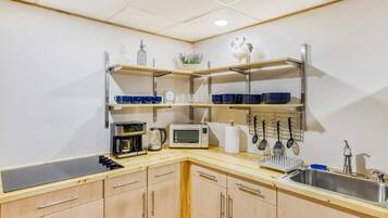 Eine moderne Küche mit Holzausbau, einer Mikrowelle, einer Kaffeemaschine und Regalen mit blauem Geschirr.