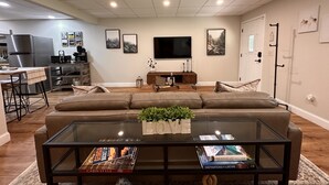 A modern living room with a sectional sofa, a coffee table, and a TV. There is a kitchen area with a refrigerator and a microwave. - Ellijay Mountain Escape with Private Pool, Fire Pit, & BBQ! (Ellijay)