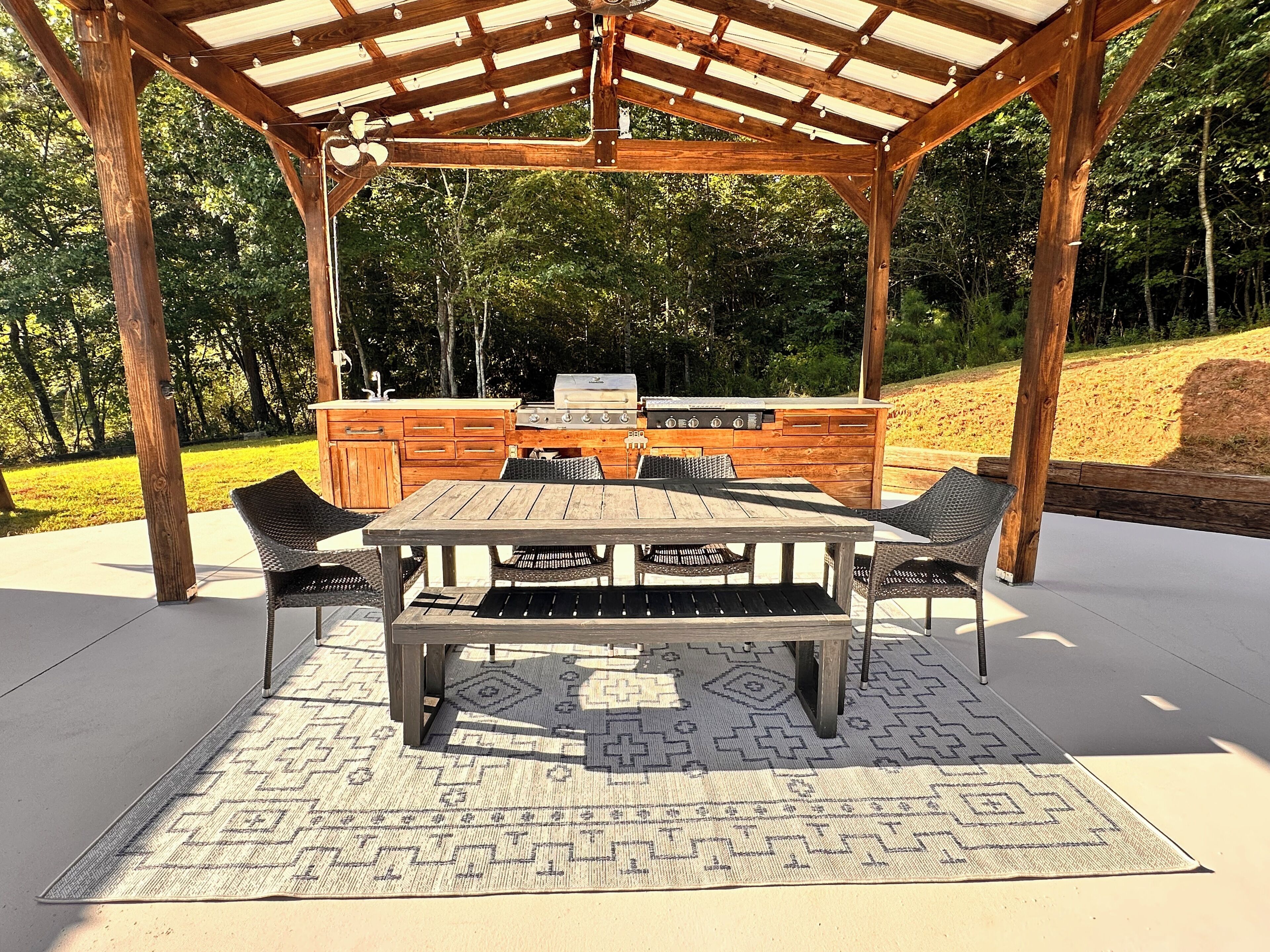 An outdoor patio with a wooden pergola, a grill, a table, and chairs.