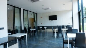 A modern dining area with glass walls, black chairs, and white tables. - Double J Hotel (Chiang Mai)